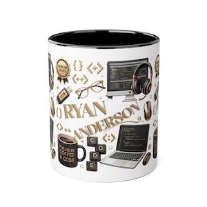 May include: A white ceramic mug with a black interior featuring a gold and black graphic pattern of computer equipment, glasses, code brackets, and the name RYAN ANDERSON. A small black mug with the text FUELLED BY COFFEE & CODE is also visible.