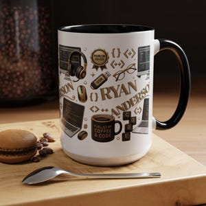 May include: A white ceramic mug with a black interior and handle, featuring a pattern of gold and black computer-themed icons including headphones, a USB drive, glasses, laptops, and a mug labeled "FUELLED BY COFFEE & CODE" with the name RYAN ANDERSON.