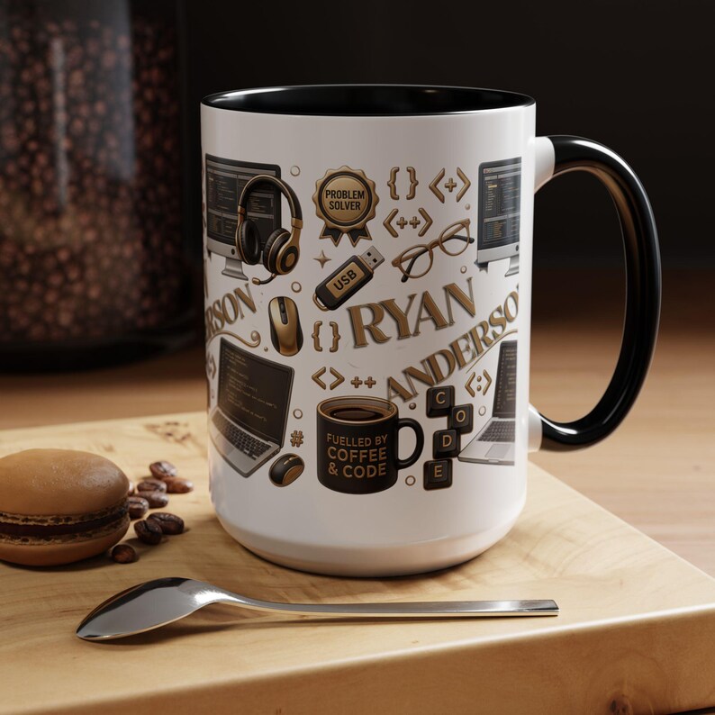 May include: A white ceramic mug with a black interior and handle, featuring a pattern of gold and black computer-themed icons including headphones, a USB drive, glasses, laptops, and a mug labeled "FUELLED BY COFFEE & CODE" with the name RYAN ANDERSON.