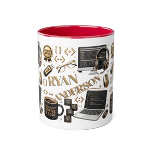 May include: A white ceramic mug with a bright red interior featuring a graphic pattern of gold and black computer-themed icons, including a laptop, monitor, headphones, glasses, and keyboard keys. The name RYAN ANDERSON is printed in gold.