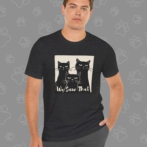 May include: A dark heather grey t-shirt with a graphic of three black cats looking at the viewer. The text "We Saw That" is printed below the cats.
