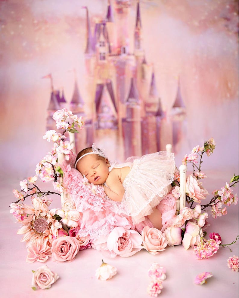 May include: A sleeping baby wearing a white lace dress and a headband, lying in a pink and white flower-filled bed with a white wooden frame. The background is a pink and purple castle.
