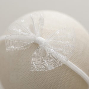 May include: White headband with a white tulle bow. The bow has a delicate, dotted pattern.