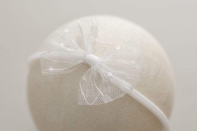 May include: White headband with a white tulle bow. The bow has a delicate, dotted pattern.