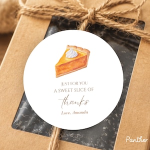 May include: A circular white sticker featuring a watercolor illustration of a slice of pumpkin pie with whipped cream. The text reads: JUST FOR YOU A SWEET SLICE OF thanks Love, Amanda. The sticker is placed on a brown cardboard gift box.