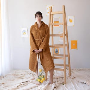 Model in the mustard waffle housecoat holding a lemon net bag by a ladder – elegant cotton waffle housecoat