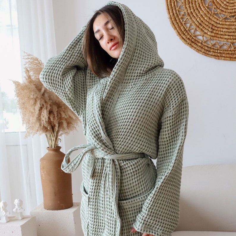 Model with the hood up in a sage green waffle robe, hand resting on the hood, waist tie fastened – elegant cotton waffle housecoat