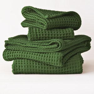May include: A stack of six green waffle-weave towels. The towels are folded and stacked on top of each other. The towels are a solid, deep green color. The towels are made of a textured material.