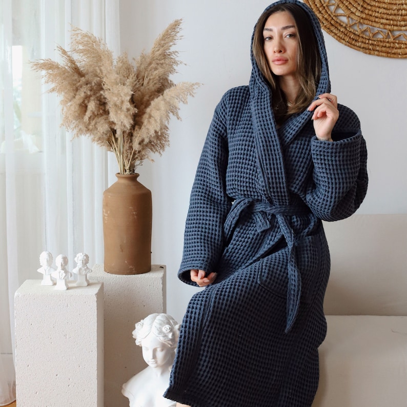 Model standing with the hood up in a dark navy waffle robe, terracotta vase with pampas grass in the background – elegant cotton waffle housecoat