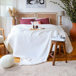 May include: White waffle knit throw blanket on a bed with a wooden headboard and a book titled "Kinfolk" on a wooden stool.