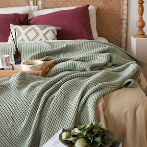 May include: A green waffle weave throw blanket draped over a bed with a wooden headboard and pillows. The blanket is soft and textured, and it would be perfect for adding a touch of warmth and comfort to any room.