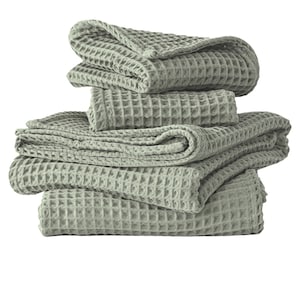 May include: A stack of four sage green waffle weave towels. The towels are folded and stacked on top of each other.