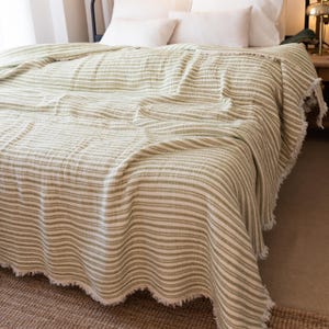 May include: A green and white striped throw blanket with a fringed edge. The blanket is draped over a bed with white pillows.