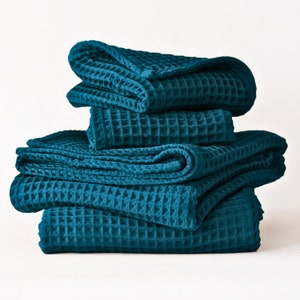 May include: A stack of four teal waffle weave towels folded neatly. The towels are made of a soft, absorbent material and are perfect for drying off after a bath or shower.