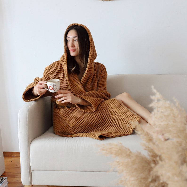 Model sitting on a sofa with the hood up in a camel brown waffle robe, holding a mug – elegant cotton waffle housecoat