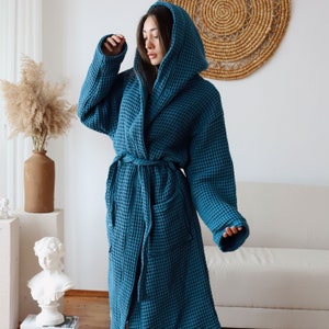 Model standing with the hood up in a teal blue waffle robe, arm raised to show the roomy sleeve – elegant cotton waffle housecoat