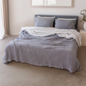 May include: A grey and white waffle weave throw blanket with a fringed edge is draped over a bed with grey and white pillowcases.