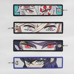 Könnte beinhalten: Vier farbenfrohe Schlüsselanhänger mit Nahaufnahmen von Anime-Augen. Jeder Schlüsselanhänger hat einen schwarzen Rand und einen silbernen Metallring.