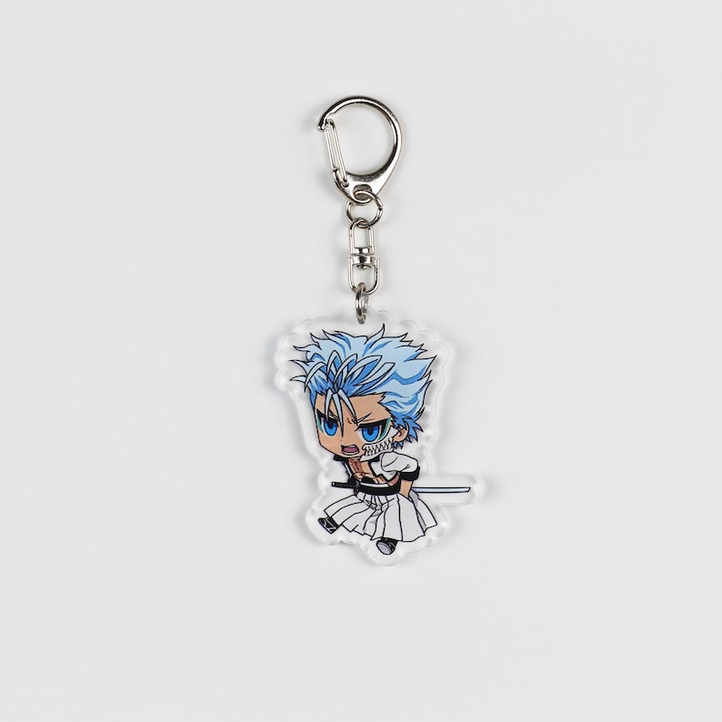 Puede incluir: Un llavero de acr&iacute;lico transparente con un personaje de anime de estilo chibi con cabello azul, un atuendo blanco y negro y una espada. El personaje tiene una expresi&oacute;n seria y sostiene la espada en su mano derecha.