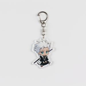 Puede incluir: Un llavero con un personaje de anime blanco y negro con una cadena plateada. El personaje tiene el pelo blanco, los ojos azules y lleva un atuendo blanco y negro.