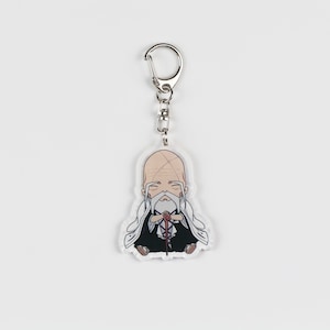 Puede incluir: Un llavero con un personaje de anime blanco y negro con una cadena plateada. El personaje es un hombre con barba blanca y una t&uacute;nica blanca. Est&aacute; sosteniendo un bast&oacute;n en sus manos.