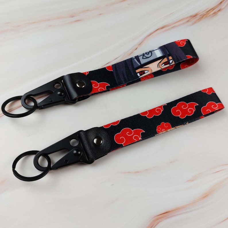 May include: Two fabric wristlet keychains featuring a black background with a repeating red cloud pattern. One keychain displays a partial anime character face with red eyes and a headband. Both include a black metal lobster clasp and a split ring.