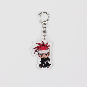 Puede incluir: Un llavero de acr&iacute;lico transparente con un personaje de anime de pelo rojo que lleva una cinta blanca en la cabeza y un atuendo blanco y negro. El llavero tiene un anillo de metal plateado.