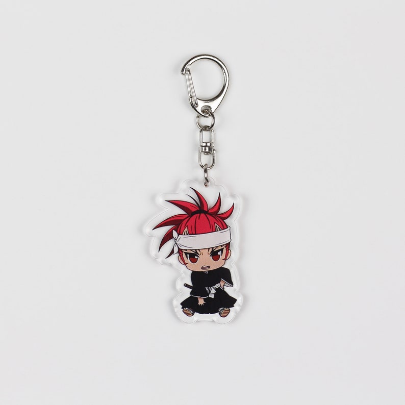 Puede incluir: Un llavero de acr&iacute;lico transparente con un personaje de anime de pelo rojo que lleva una cinta blanca en la cabeza y un atuendo blanco y negro. El llavero tiene un anillo de metal plateado.