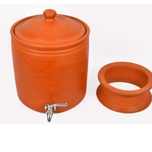 K&ouml;nnte beinhalten: Ein Terrakotta-Wasserkrug mit Deckel und einem Hahn. Der Krug steht auf einer wei&szlig;en Oberfl&auml;che. Der Krug ist aus Ton gefertigt und hat eine nat&uuml;rliche, erdige Farbe.