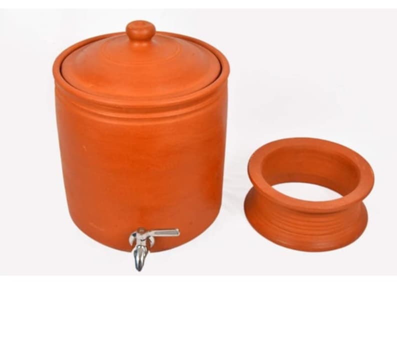 K&ouml;nnte beinhalten: Ein Terrakotta-Wasserkrug mit Deckel und einem Hahn. Der Krug steht auf einer wei&szlig;en Oberfl&auml;che. Der Krug ist aus Ton gefertigt und hat eine nat&uuml;rliche, erdige Farbe.
