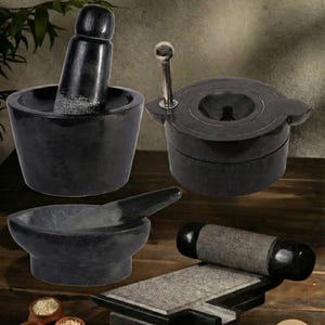 May include: A selection of black stone kitchen implements, including a mortar and pestle, a grinding stone, and a spice grinder. The image also shows small clay pots with spices and garlic cloves.
