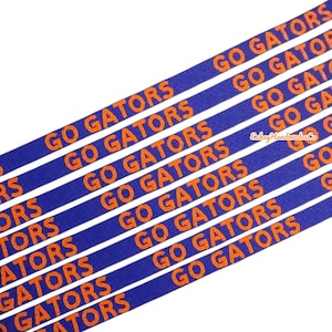 Puede incluir: Cinta azul con la frase "GO GATORS" en naranja repetida en diagonal. La cinta es de color azul liso con el texto en naranja contrastante.