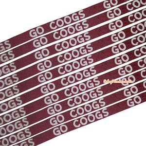 Puede incluir: Primer plano de cinta de color granate con la inscripción blanca "GO COOGS". Las líneas paralelas crean un patrón repetitivo. El texto es claro y legible, ideal para proyectos de manualidades o temáticos deportivos.