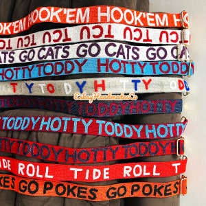 May include: A collection of colourful beaded belts with various phrases, including "Hook 'em", "Cats Go", "Hotty Toddy", "Roll Tide", and "Pokes Go".