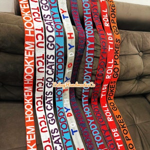 May include: A collection of colourful woven straps with various text printed on them, including "HOOK'EM", "TCU", "GO CATS", "HOTTY TODDY", "TIDE ROLL", and "GO POKES".