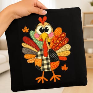 Könnte beinhalten: Ein schwarzes quadratisches Kissen mit einem farbenfrohen Patchwork-Truthahndesign. Der Truthahn hat einen gelben Schnabel, eine rote Wamme und einen Patchwork aus orangefarbenen, roten, grünen und gelben Federn. Zwei orangefarbene Ahornblätter sind ebenfalls zu sehen.