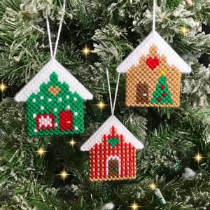 Könnte beinhalten: Drei handgemachte Weihnachtsbaumschmuckstücke in Form von Häusern. Die Häuser sind mit rotem, grünem und weißem Garn verziert und haben ein schneebedecktes weißes Dach. Der Schmuck hängt an einem grünen Weihnachtsbaum.