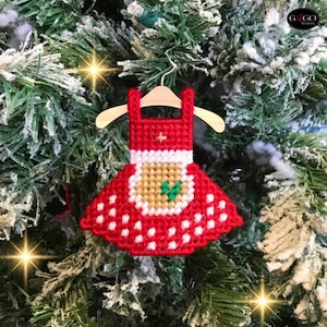 May include: Red and white felt Christmas ornament shaped like a dress with a green and brown felt applique. The ornament is hanging from a wooden hanger.