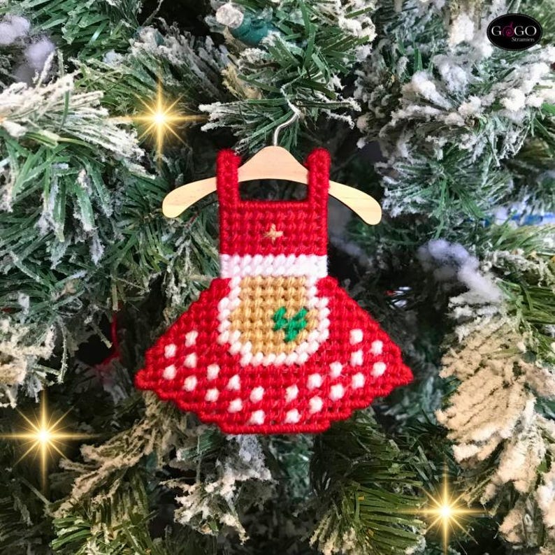 May include: Red and white felt Christmas ornament shaped like a dress with a green and brown felt applique. The ornament is hanging from a wooden hanger.