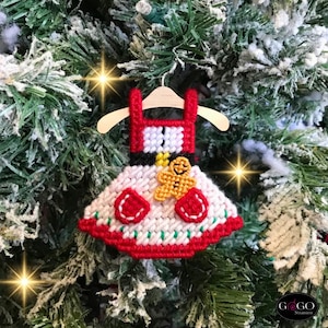 May include: A red and white Christmas ornament shaped like a dress with a gingerbread person on the front. The ornament is hanging on a Christmas tree.