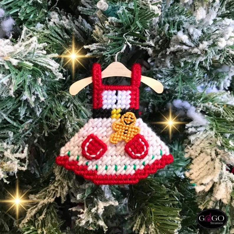 May include: A red and white Christmas ornament shaped like a dress with a gingerbread person on the front. The ornament is hanging on a Christmas tree.