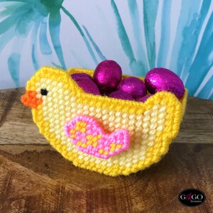 May include: A yellow crocheted chick shaped basket filled with pink foil-wrapped chocolate eggs. The chick has a pink heart on its chest.