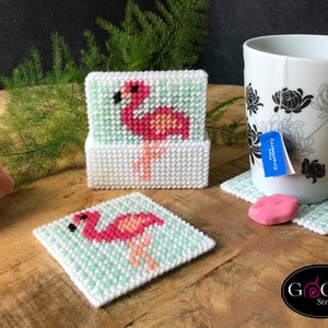 May include: Set of four pink flamingo coasters with green accents. The coasters are made of plastic canvas and are perfect for adding a touch of tropical flair to your home decor.
