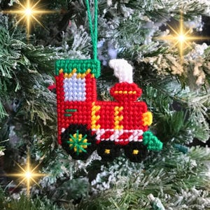 Puede incluir: Un adorno de tren rojo, amarillo y blanco con un techo verde y ruedas negras. El adorno está colgado de un árbol de Navidad.