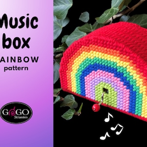 May include: A rainbow-coloured yarn craft music box with a red top and a winding key. The music box is shaped like a half-circle and has a small hole in the centre. The music box is sitting on a green leafy branch.