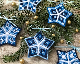 May include: Five blue and white star-shaped ornaments with a snowflake design. The ornaments are made of yarn and have a blue ribbon attached to each.