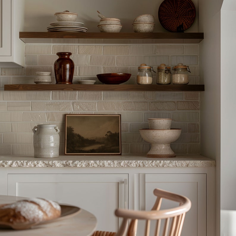 Puede incluir: Una cocina blanca con estantes de madera llenos de varios cuencos de cer&aacute;mica, tarros y un jarr&oacute;n. Los estantes est&aacute;n contra una pared de ladrillo blanco. Un cuadro enmarcado de un paisaje cuelga de la pared. Una hogaza de pan se encuentra sobre una mesa de madera en primer plano.