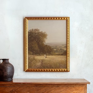 May include: A framed landscape painting with a gold ornate frame. The artwork depicts a field with a path leading to a figure in the distance, surrounded by trees and a distant view of rolling hills. The painting has a vintage aesthetic.