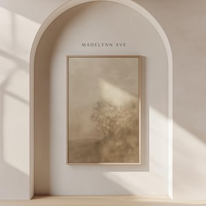 May include: A framed landscape art print featuring a muted color palette of beige and brown tones. The artwork depicts a tree in a misty field. The text "MADELYNN AVE" is above the frame, set against a white arched wall.