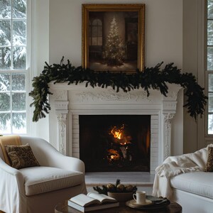 May include: A white fireplace with a roaring fire inside. A green garland is draped across the mantelpiece, and a framed painting of a snowy forest scene hangs above the fireplace.